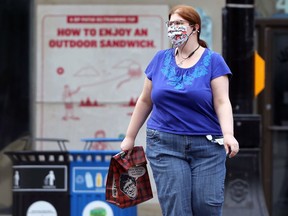 A woman wearing a mask carries a takeout bag across Main Street in Winnipeg on Monday, July 26, 2021.