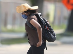 A person wears a mask and a large straw hat while crossing a street in Winnipeg on Friday, July 30, 2021.