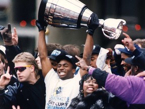 Toronto Argonaut Raghib (Rocket) Ismail raises the Grey Cup high above the crowd during parade festivities as his mother Fatma (immediate right), smiles in Toronto, Ontario on Tuesday, Nov. 26, 1991.