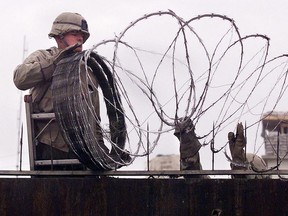 In this file photo, a U.S. Marine is given a hand using barbed wire to secure the walls of the U.S. embassy in Kabul, Afghanistan, Jan. 11, 2002.