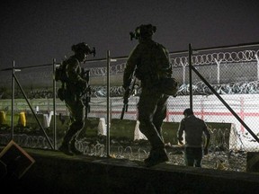 In this picture taken in the late hours on August 22, 2021 British and Canadian soldiers stand guard near a canal as Afghans wait outside the foreign military-controlled part of the airport in Kabul on August 23, 2021, hoping to flee the country following the Taliban's military takeover of Afghanistan.