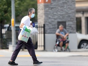 A person wears a mask while crossing a street in downtown Winnipeg on Tuesday. Chris Procaylo/Winnipeg Sun