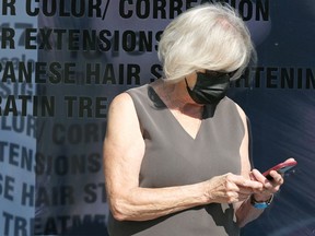 A woman wearing a mask looks at her phone outside a hair salon on Corydon Avenue in Winnipeg on Tuesday, Aug. 31, 2021.