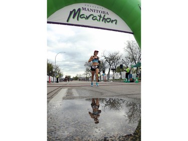 Erica Sharfstein is reflected in a puddle as she crosses the finish line of her half marathon at the Manitoba Marathon on Chancellor Matheson Road in Winnipeg on Sunday, Sept. 5, 2021.