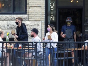 Masked people bring food and drinks out onto the patio of a sandwich shop in the Exchange District of Winnipeg on Monday, Sept. 6, 2021.