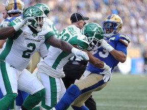 Winnipeg Blue Bombers RB Andrew Harris (right) throws Saskatchewan Roughriders DB Christian Campbell to the ground by the helmet as DL Micah Johnson tries to get at Harris during a fracas at the Banjo Bowl in Winnipeg on Saturday, Sept. 11, 2021.