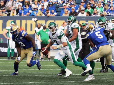 Saskatchewan Roughriders QB Cody Fajardo (centre) scrambles in the pocket with pressure from Winnipeg Blue Bombers DE Jonathan Kongbo (left) and Willie Jefferson (right) during the Banjo Bowl in Winnipeg on Saturday, Sept. 11, 2021.