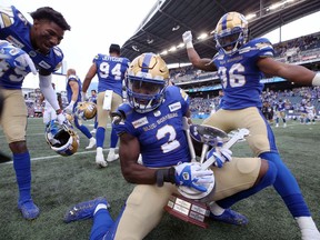 DeAundre Alford (left) and Jontrell Rocquemore (right) help Jonathan Kongbo celebrate with the Banjo Bowl trophy after beating the Saskatchewan Roughriders in Winnipeg on Saturday, Sept. 11, 2021.