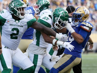 Winnipeg Blue Bombers RB Andrew Harris (right) throws Saskatchewan Roughriders DB Christian Campbell to the ground by the helmet as DL Micah Johnson tries to get at Harris during a fracas at the Banjo Bowl in Winnipeg on Saturday, Sept. 11, 2021.