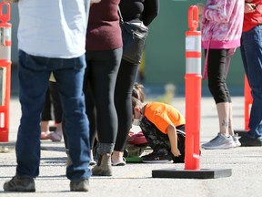 Children busy themselves on the concrete while people wait in line at a COVID-19 testing site on Portage Avenue in Winnipeg on Mon., Sept. 13, 2021. KEVIN KING/Winnipeg Sun/Postmedia Network