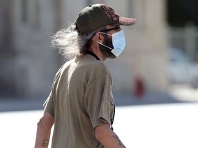 Sun lights up the hair of a man wearing a mask as he crosses Portage Avenue in Winnipeg on Monday. Manitoba averaged 70 new cases of COVID-19 a day since last Thursday.