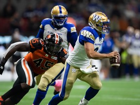Winnipeg Blue Bombers quarterback Zach Collaros (right) eludes B.C. Lions' Tim Bonner (45) during the first half of their game in Vancouver, on Friday,