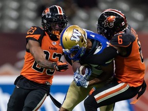 Winnipeg Blue Bombers' Kenny Lawler, centre, is tackled by B.C. Lions' T.J. Lee (right) and Anthony Thompson after making a reception in Vancouver Friday night. THE CANADIAN PRESS/Darryl Dyck