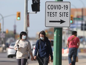 People wear masks while walking past a sign for a COVID-19 test site in Winnipeg on Tuesday, Oct. 5, 2021.