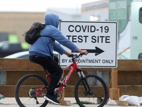 A person rides a bicycle past a sign for a Covid-19 test site in Winnipeg on  Wednesday, October 13, 2021. Chris Procaylo/Winnipeg Sun