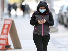 A woman wearing a mask uses her phone while walking in downtown Winnipeg on Tues., Oct. 12, 2021. KEVIN KING/Winnipeg Sun/Postmedia Network