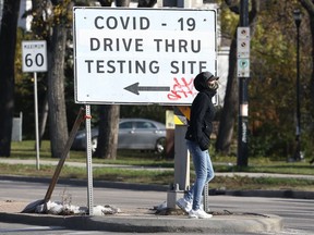 A woman stops on the median near a sign for a COVID-19 testing site on Main Street in Winnipeg on Mon., Oct. 18, 2021. KEVIN KING/Winnipeg Sun/Postmedia Network