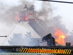 Firefighters in a ladder truck work on hotspots of a fire in a warehouse behind a storefront once owned by Peter Nygard at Notre Dame Avenue and Clifton Street in Winnipeg on Tuesday, Oct. 19, 2021.