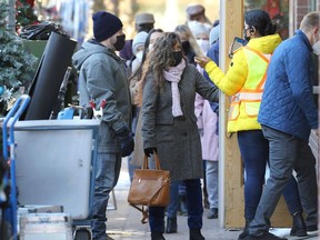 People wearing masks outside a Bannatyne Avenue location being used for 'Tis the Season to be Merry, a Hallmark Movie of the Week starring Rachael Leigh Cook which is filming in Winnipeg, on Monday, Oct. 25, 2021.