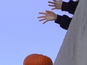 A person drops a pumpkin off a parkade roof in Winnipeg on Saturday, Nov. 6, 2021, as part of a pumpkin composting effort.