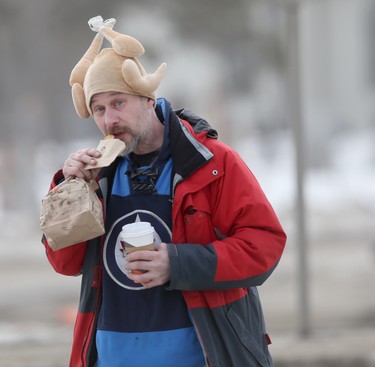 A person wearing a hat that looks like a roast chicken eats food while crossing a street, in Winnipeg on February 24. Chris Procaylo/Winnipeg Sun