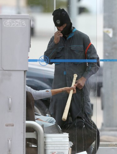 A person adjusts their ski mask in a bus shack while another person holds their bat, in Winnipeg on August 12. Chris Procaylo/Winnipeg Sun