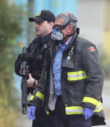A Winnipeg fire fighter wears gloves, eye protection and a high quality mask while a police officer holds an automatic weapon at the scene of an apparent shooting on October 27. Chris Procaylo/Winnipeg Sun