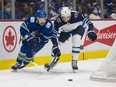 Winnipeg Jets defenceman Brenden Dillon (5) and Vancouver Canucks forward Conor Garland (8) reach for the loose puck in the first period at Rogers Arena in Vancouver on Dec. 10, 2021.