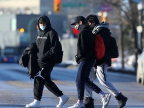 Three people wear masks while walking across a street in Winnipeg on Friday, Dec. 3, 2021.