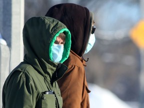 Two people wear masks while crossing a street in Winnipeg on Saturday, Jan. 1, 2022.