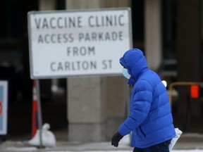 A person wears a mask while walking past a sign for a COVID-19 vaccine clinic in Winnipeg on Tuesday, Jan. 11, 2022.