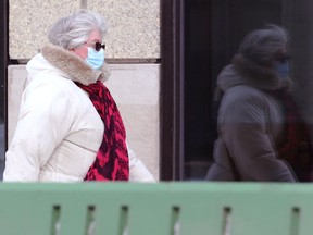 A woman wearing a mask is reflected in a window on Portage Avenue near Main Street in Winnipeg on Monday, Jan. 17, 2022.