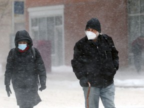 People wearing masks cross a downtown Winnipeg street in heavy blowing snow on Tuesday, Jan. 18, 2022.