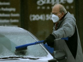 A person wears a mask while brushing snow from a vehicle in Winnipeg on Friday, Jan. 21. 2022.