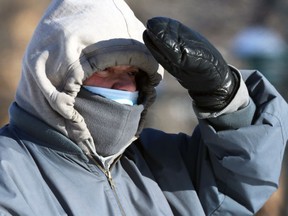 A man wearing a mask uses a mitt to block the sun in Osborne Village in Winnipeg on Monday, Jan. 23, 2022.