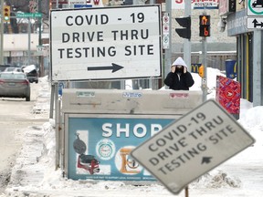A person adjusts their mask near signage for the COVID-19 drive-thru testing site on Main Street in Winnipeg on Sunday, Jan. 30, 2022.