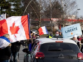 Participants of the "Freedom Convoy" (Convoi de la Liberte) wave flags and hold up a banner as they stand on the roadside outside the Canadian memorial of Vimy, northern France on February 13, 2022. - Thousands of protesters in convoys, inspired by Canadian truckers paralysing border traffic with the US, were heading to Paris from across France on February 11, with some hoping to blockade the capital in opposition to Covid-19 restrictions despite police warnings to back off. The protesters include many anti-Covid vaccination activists, but also people protesting against fast-rising energy prices that they say are making it impossible for low-income families to make ends meet. (Photo by THOMAS LO PRESTI / AFP) (Photo by THOMAS LO PRESTI/AFP via Getty Images)