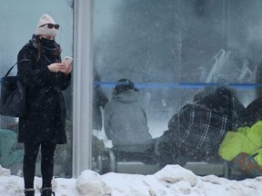 A person stands outside at a bus stop while the bus shelter is occupied by people who appear to be living there on Wednesday, Jan. 26, 2022.