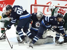 Winnipeg Jets goaltender Connor Hellebuyck (centre) covers the puck as centre Pierre-Luc Dubois (second left) and defenceman Brenden Dillon (second right) deal with Minnesota Wild forwards Joel Eriksson Ek (left) and Jordan Greenway.