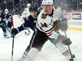 Chicago Blackhawks forward Sam Lafferty (24) shields the puck away from Winnipeg Jets defenceman Ville Heinola (14) during the first period at Canada Life Centre in Winnipeg on Feb. 14, 2022.