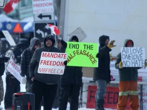 A small group of people on Broadway, in Winnipeg, with signs and flags on Wednesday, Feb. 16, 2022.