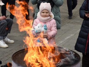 A child warms herself next to a fire as people wait for a train to Poland at the railway station of the western Ukrainian city of Lviv on March 6, 2022, 11 days after Russia launched a military invasion on Ukraine.