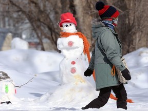 A woman wearing a face covering walks by a snowman and his sidekick on Wellington Crescent in Winnipeg on Sunday, March 13, 2022.