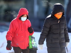 Two people wear masks while crossing a street in Winnipeg on Tuesday, March 1, 2022.