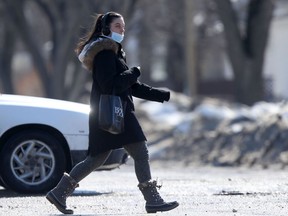 A person wears a mask while crossing a street in Winnipeg on Saturday, March 19, 2022.