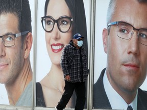 A person wears a mask while walking past large images of faces on the windows of a shop in Winnipeg. Chris Procaylo/Winnipeg Sun