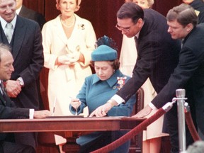 Queen Elizabeth signs Canada's constitutional proclamation in Ottawa on April 17, 1982, as Prime Minister Pierre Trudeau looks on. Michael Pitfield in glasses is showing Queen Elizabeth where to sign the document.