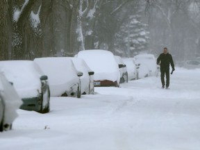 A person walks along a road beside numerous snow covered vehicles in Winnipeg on Thursday, April 14, 2022.