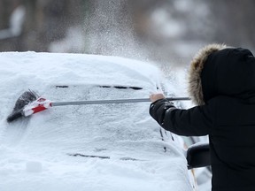 A person clears snow from a vehicle in Winnipeg after a spring storm on Friday, April 15, 2022.