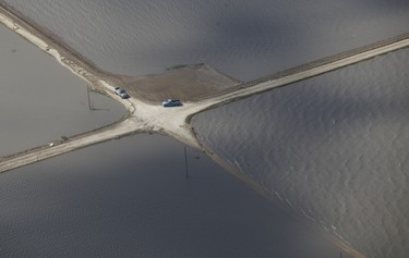 Vehicles makes it’s way down a road surrounded by water as a result of Red River flooding south of Winnipeg, Sunday, May 15, 2022. John Woods/Pool/The Canadian Press